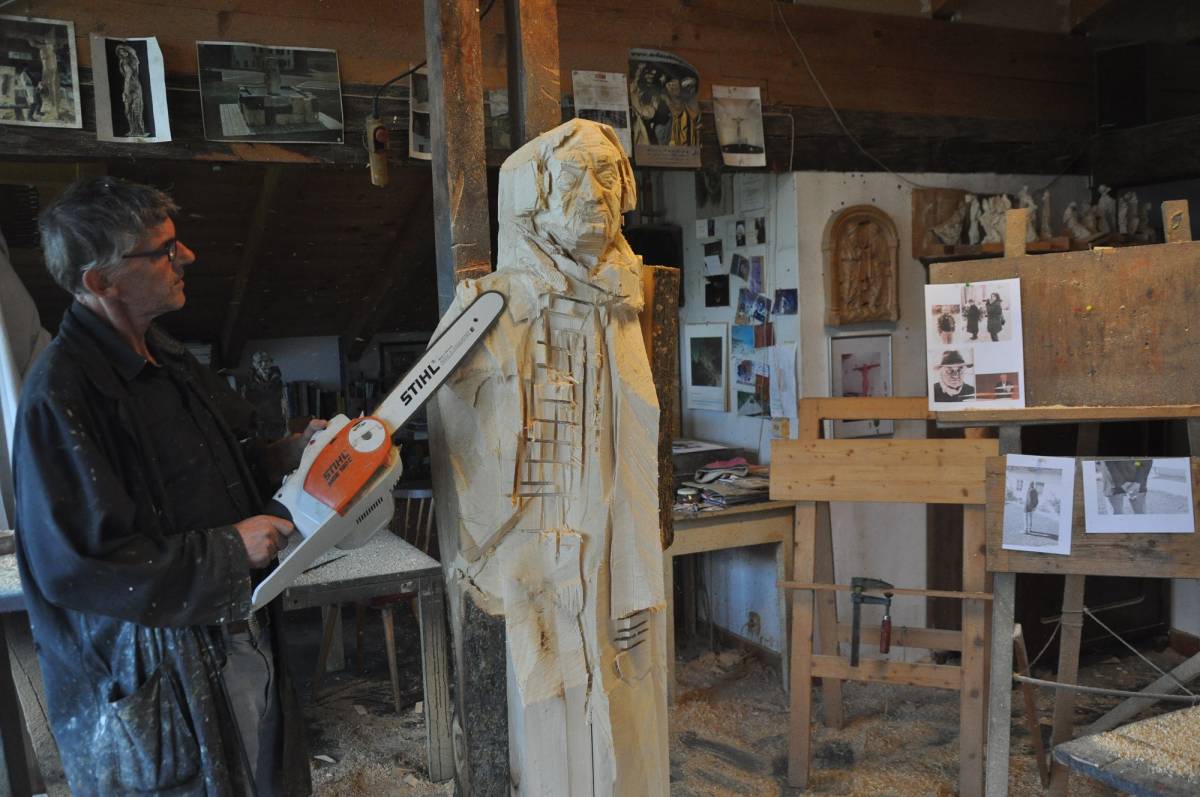 Mann mit Kettensäge an einer Llebensgroße Holzfigur arbeitend.