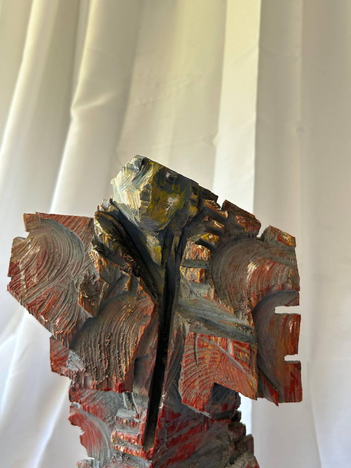 Detailaufnahme einer roten Engelsfigur aus Holz auf Metallplatte, nach rechts blickend, mit sichtbaren Kettensägespuren vor hellem Hintergrund