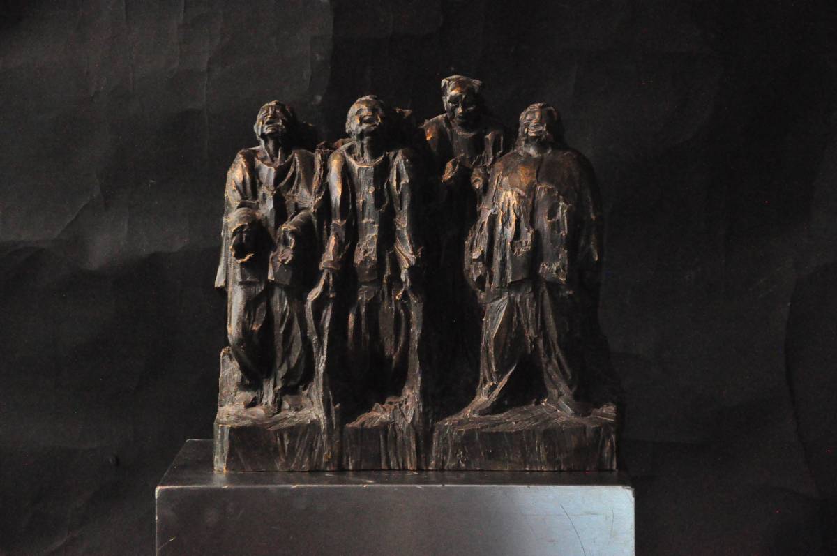 Bronzeskulptur mit vier stehenden Männern beim Singen, drei blicken nach oben, einer nach unten, dunkelbraune Oberfläche mit hellen, glänzenden Stellen an den Schultern vor dunklem Hintergrund