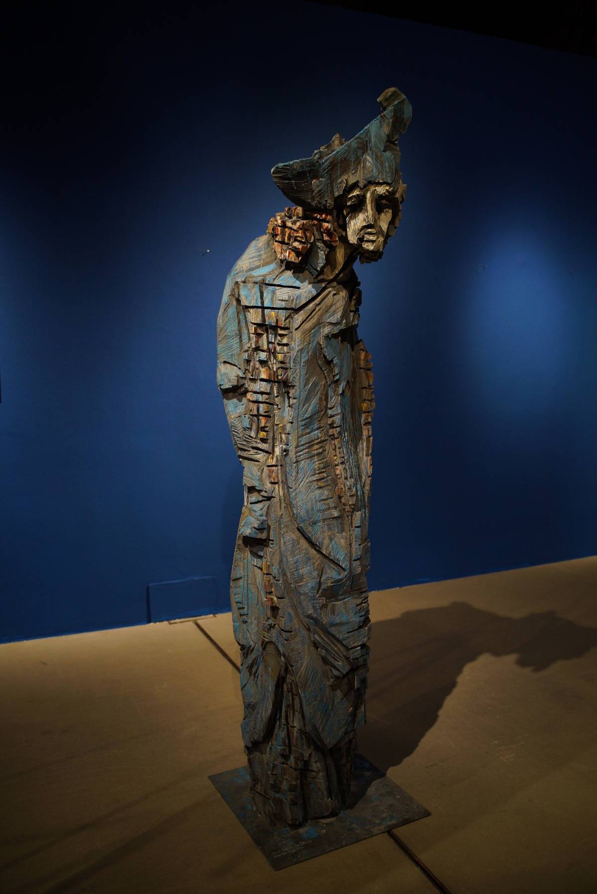 Lebensgroße Holzfigur eines Mannes mit blauen Kapitänshut, zerklüftete Kettensägespuren in Blau und Grau mit blauem Hintergrund
