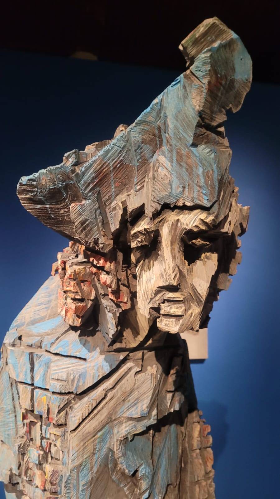Detailaufnahme eines Holzkopfes mit Kapitänshut, hohlen Augen und sichtbaren Kettensägespuren in Blau und Grau