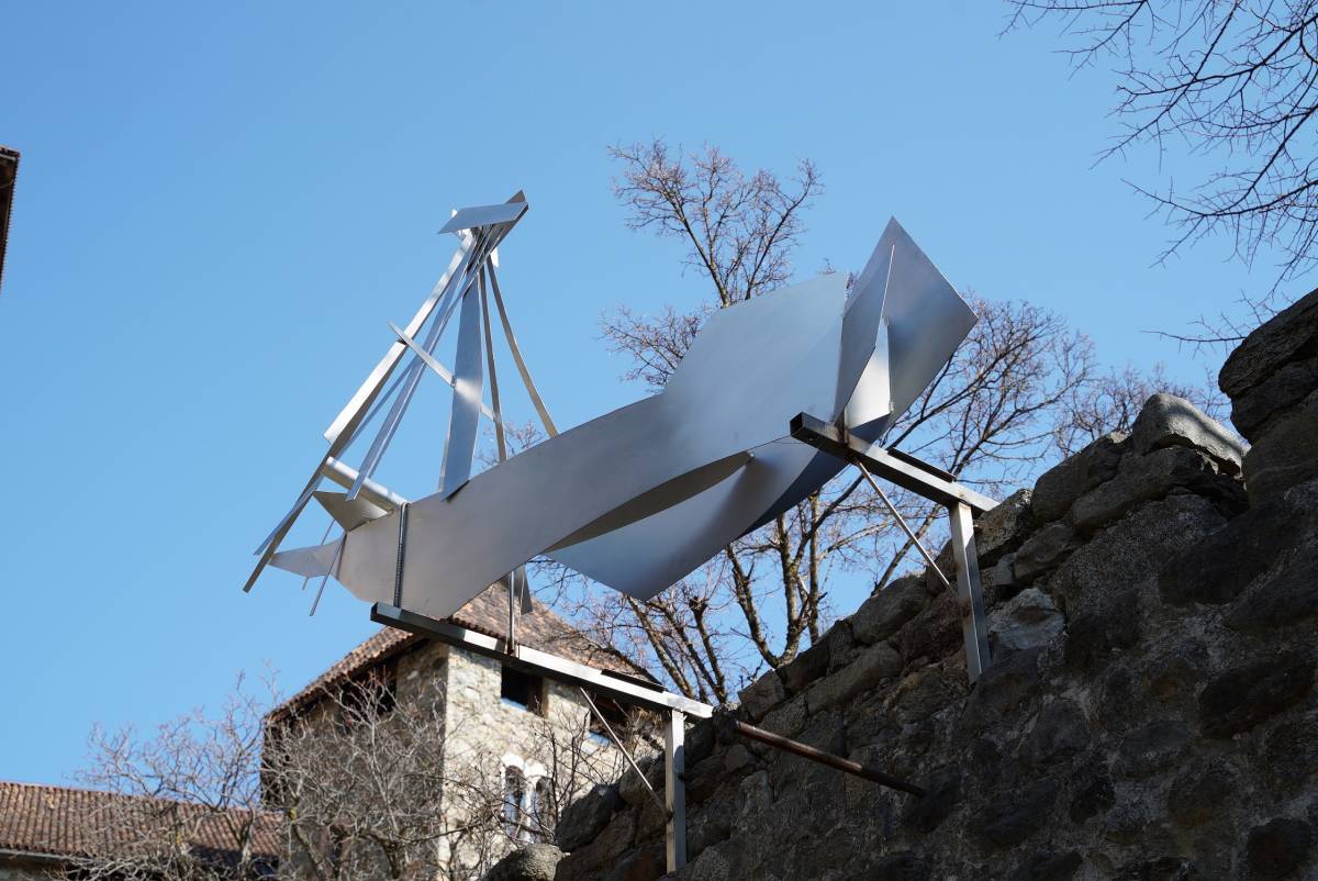 Auf einer alten Steinmauer montiertes massives 3D-Schiff aus glänzenden Aluplatten mit blauem Himmel als Hintergrund