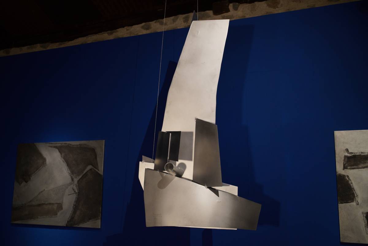 Hängendes, massives 3D-Schiff aus glänzenden Aluplatten mit angedeutetem Segel und Kanonenrohr vor blauem Hintergrund