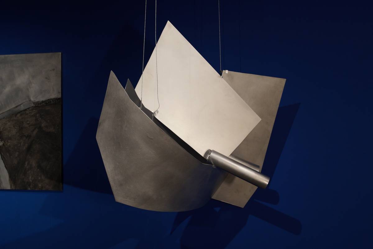 Hängendes, massives 3D-Schiff aus glänzenden Aluplatten mit angedeutetem Kanonenrohr vor blauem Hintergrund