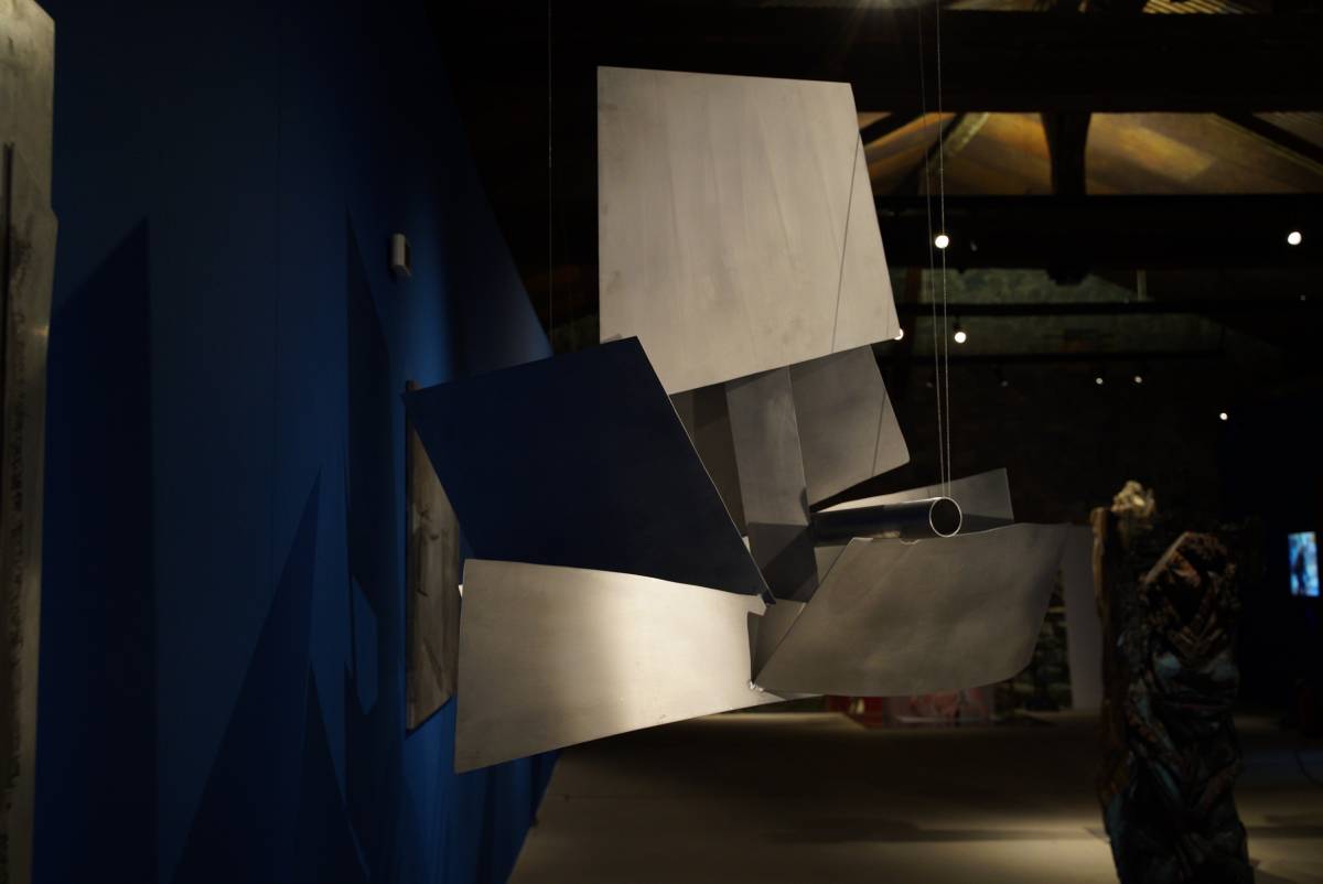 Hängendes, massives 3D-Schiff aus glänzenden Aluplatten mit angedeutetem Kanonenrohr vor blauem Hintergrund