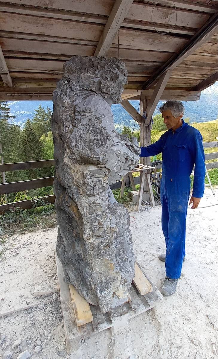Mann im blauen Overall arbeitet an einer lebensgroßen Skulptur aus hellem Stein.